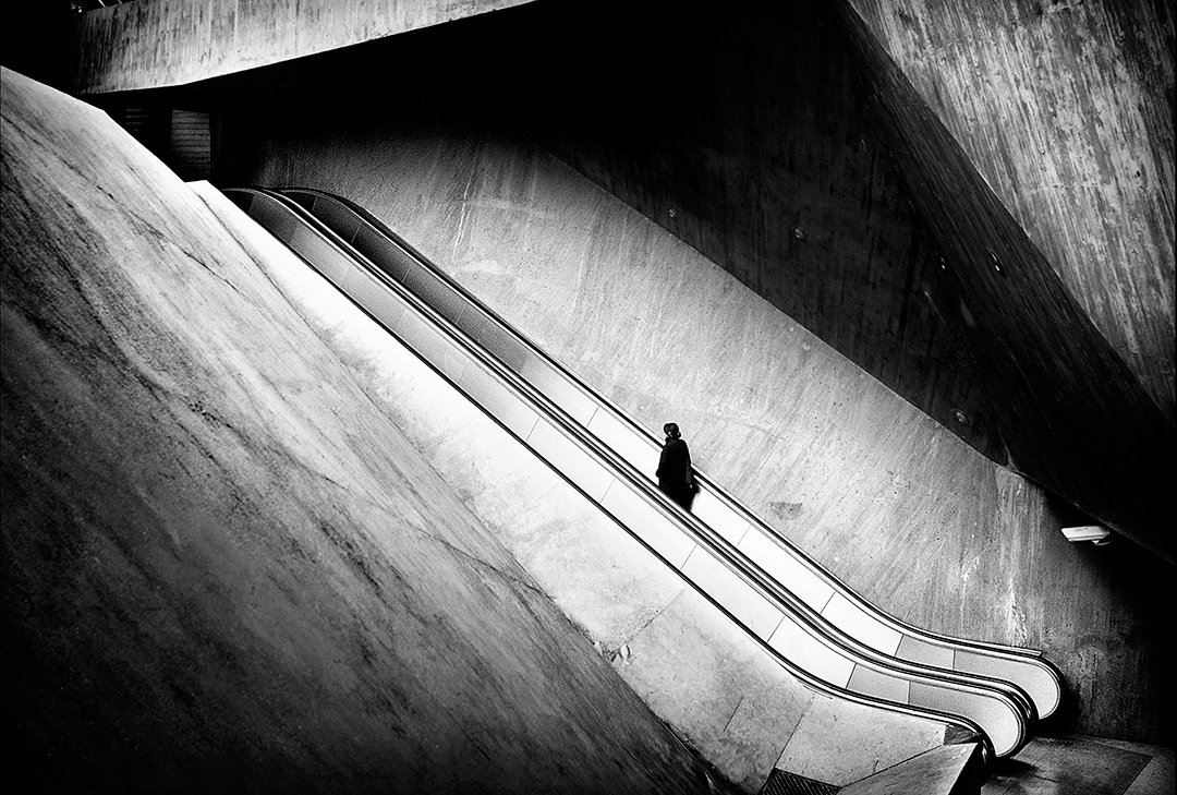 Una figura en una escalera mecánica entre grandes superficies curvas.